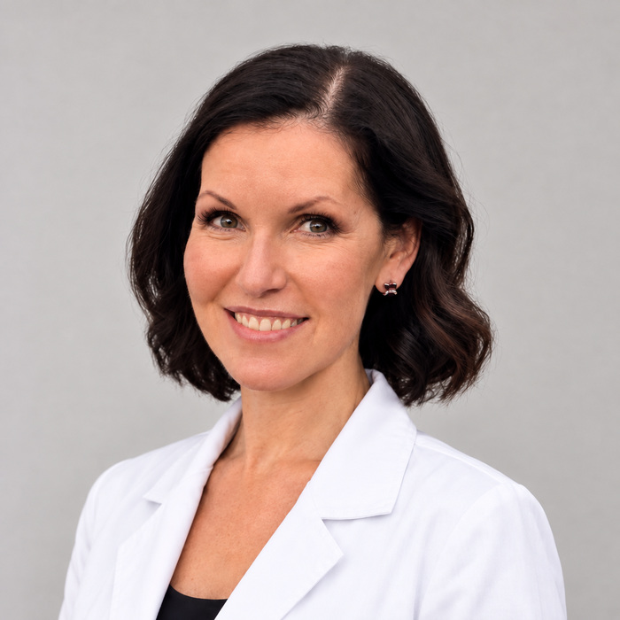 Portrait of a smiling female doctor with short dark hair in a white lab coat against a gray background
